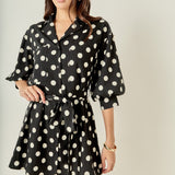 Face-forward posed view of a black and white polka dot belted shirt dress showcasing the complete look and tailored silhouette.