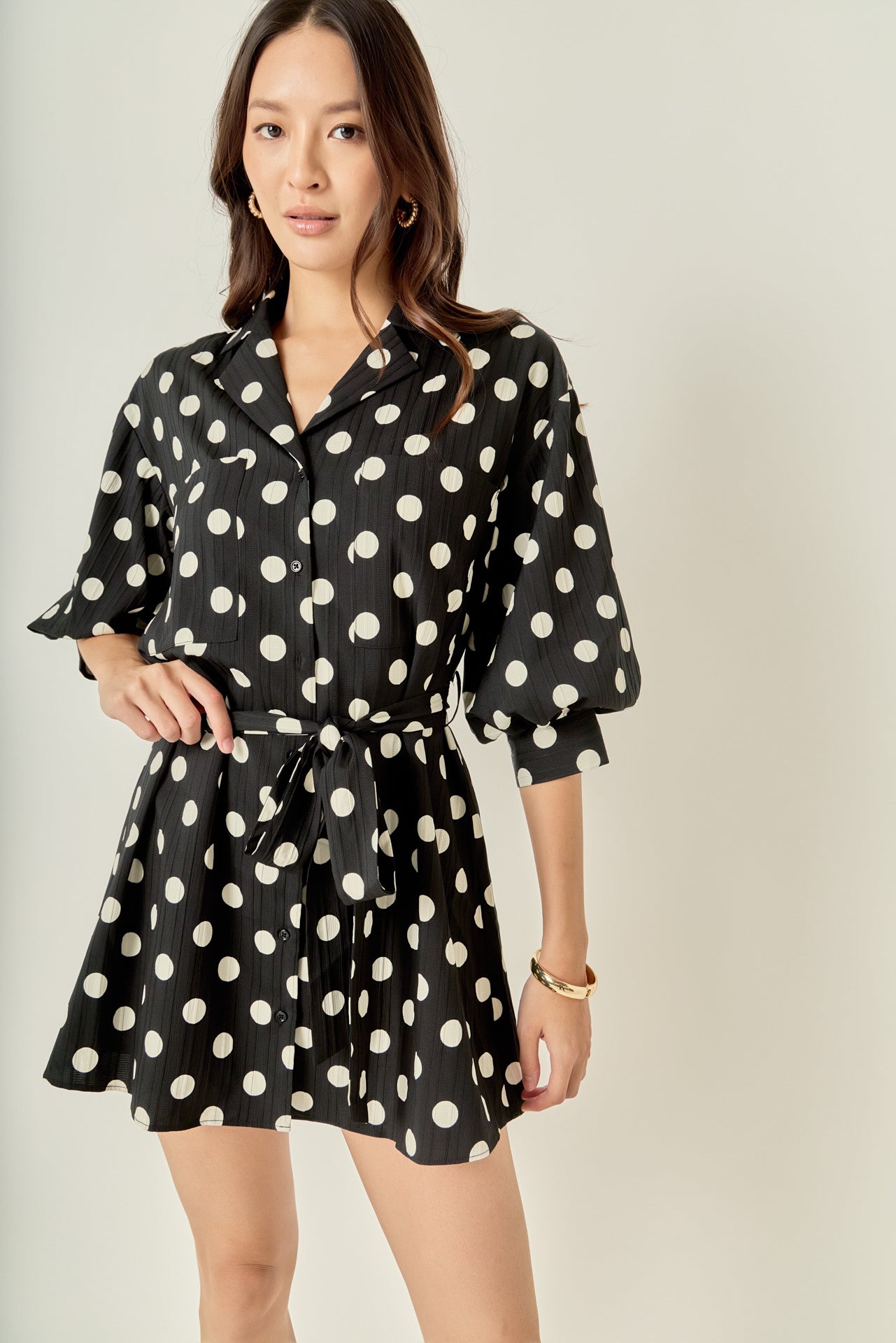 Face-forward posed view of a black and white polka dot belted shirt dress showcasing the complete look and tailored silhouette.