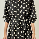 Upper body close-up view of a black and white polka dot shirt dress highlighting the notched collar, chest pockets, and front button placket.