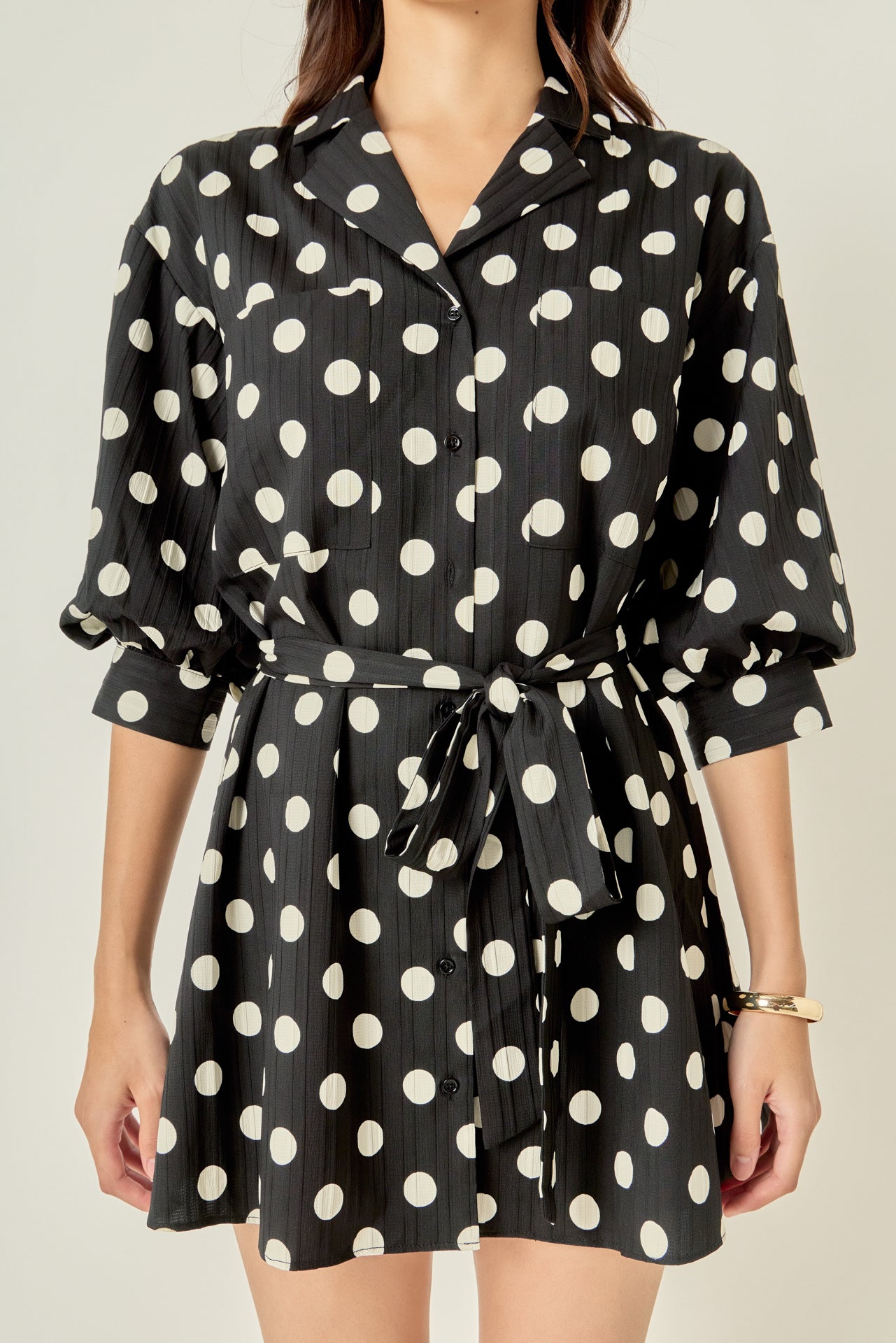 Upper body close-up view of a black and white polka dot shirt dress highlighting the notched collar, chest pockets, and front button placket.