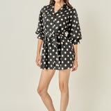 Side profile view of a black and white polka dot shirt dress showing the relaxed sleeve volume and mini-length hemline.