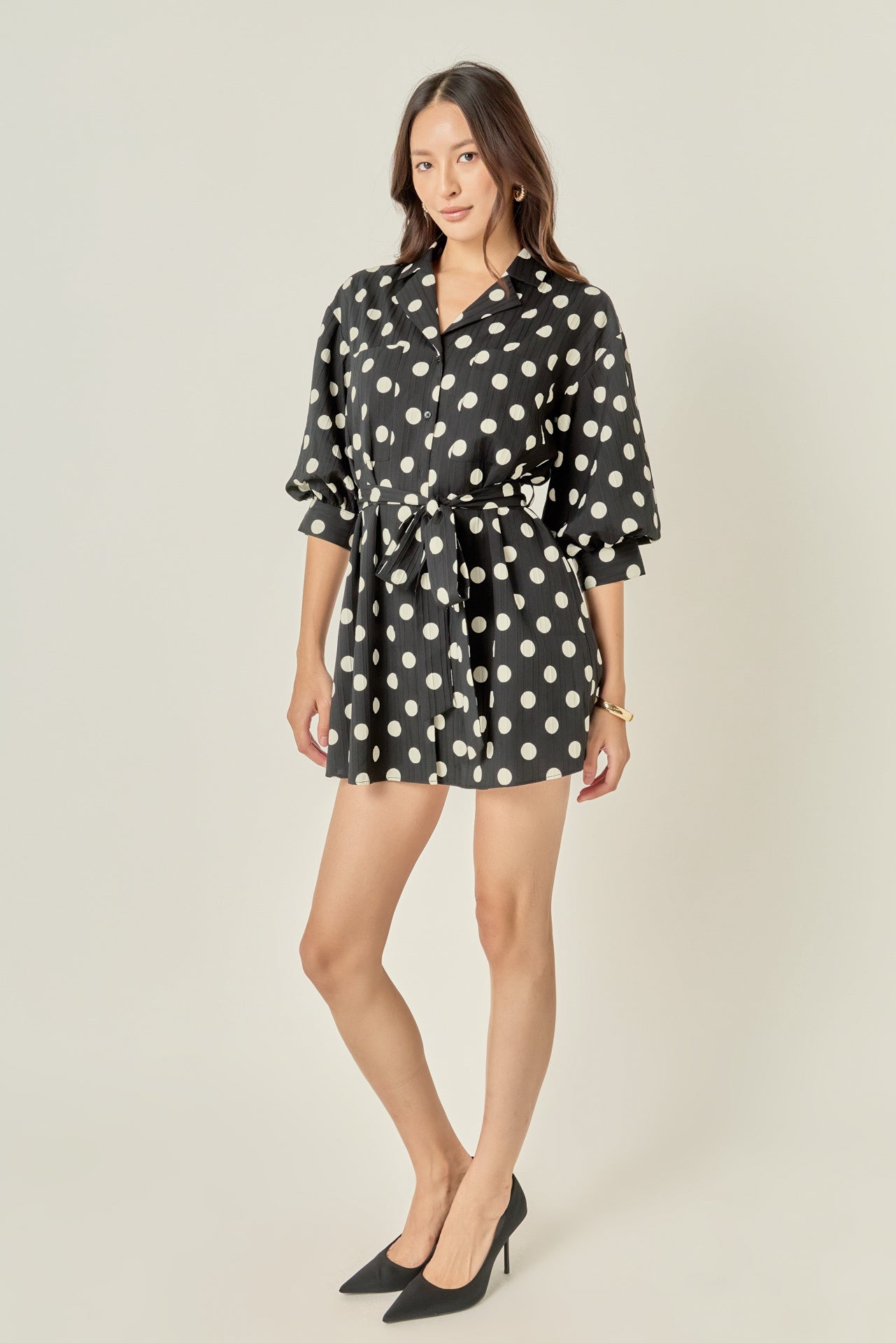 Side profile view of a black and white polka dot shirt dress showing the relaxed sleeve volume and mini-length hemline.