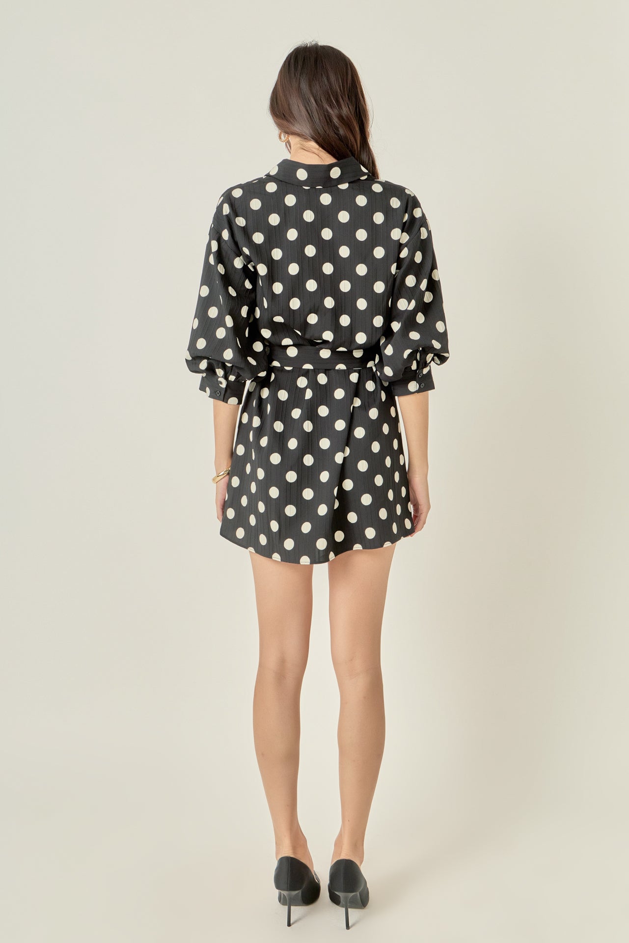 Straight-on rear view of a black and white polka dot shirt dress displaying the clean back waistline and continuous print pattern.