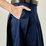 Close-up view of a navy pleated midi skirt highlighting the low-rise waistband, structured belt loops, and crisp knife pleats.