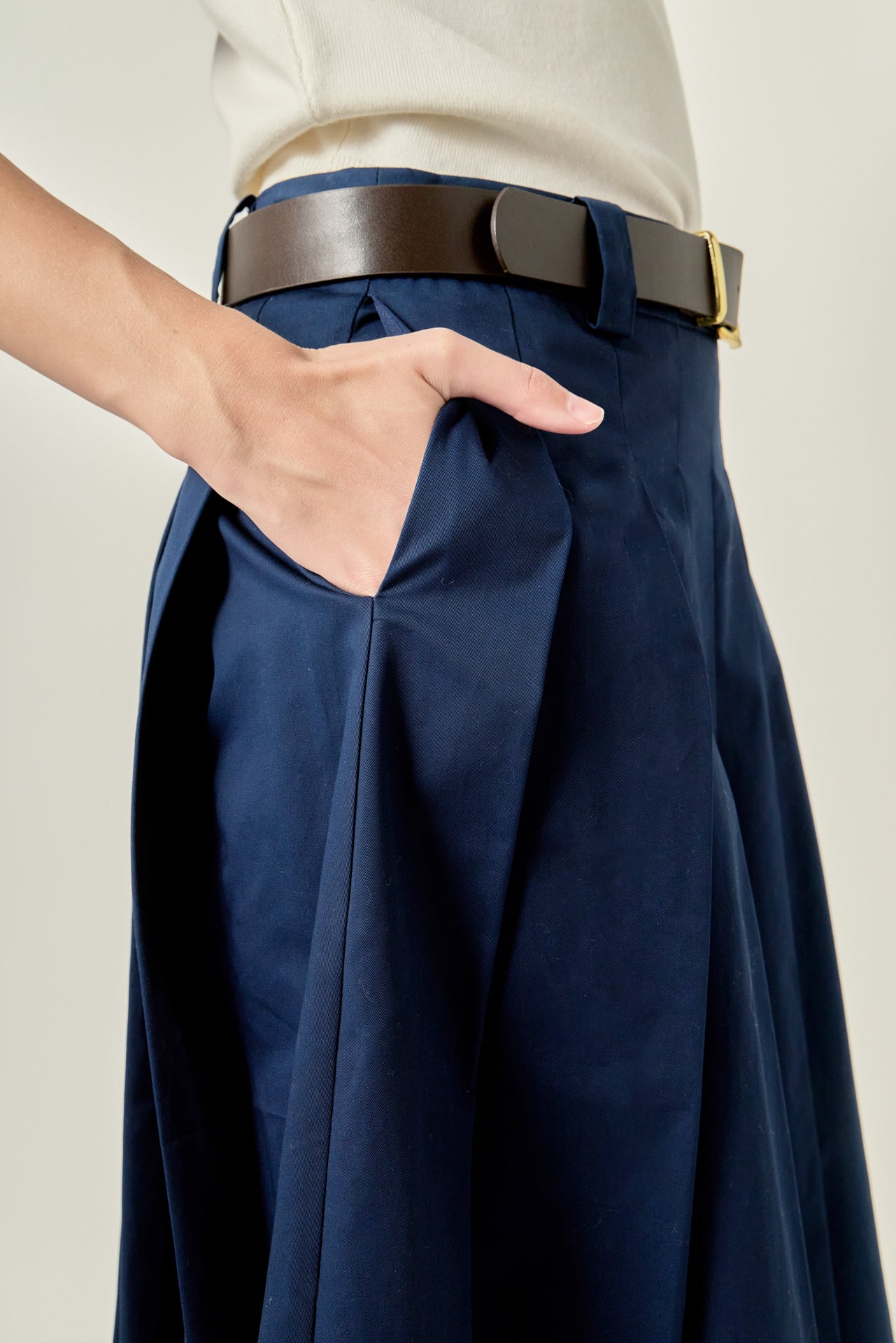 Close-up view of a navy pleated midi skirt highlighting the low-rise waistband, structured belt loops, and crisp knife pleats.