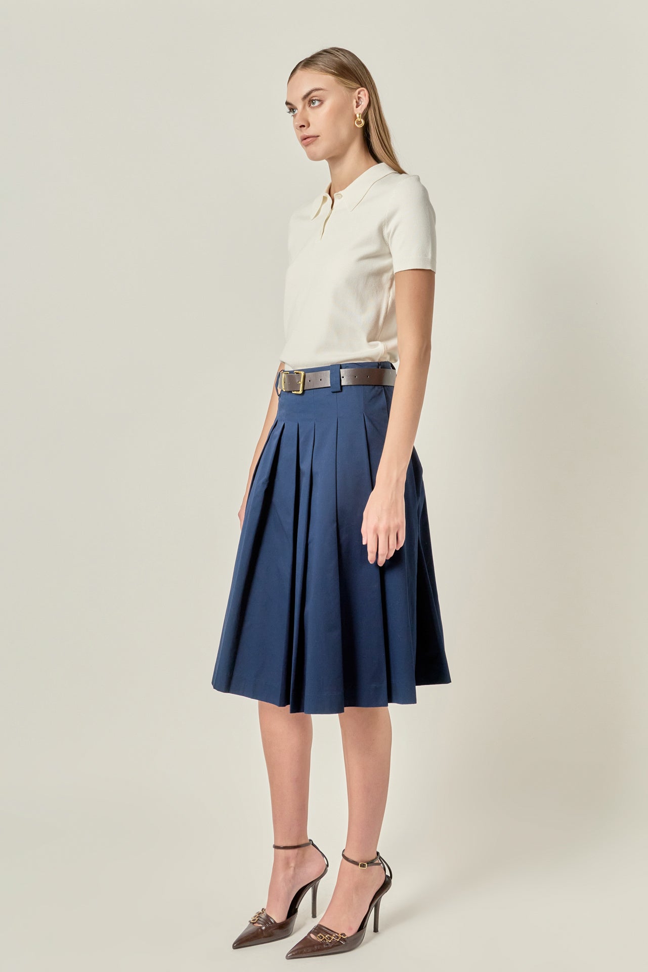 Side profile view of a navy low-waist pleated midi skirt displaying the clean side invisible zipper seam and flared silhouette.
