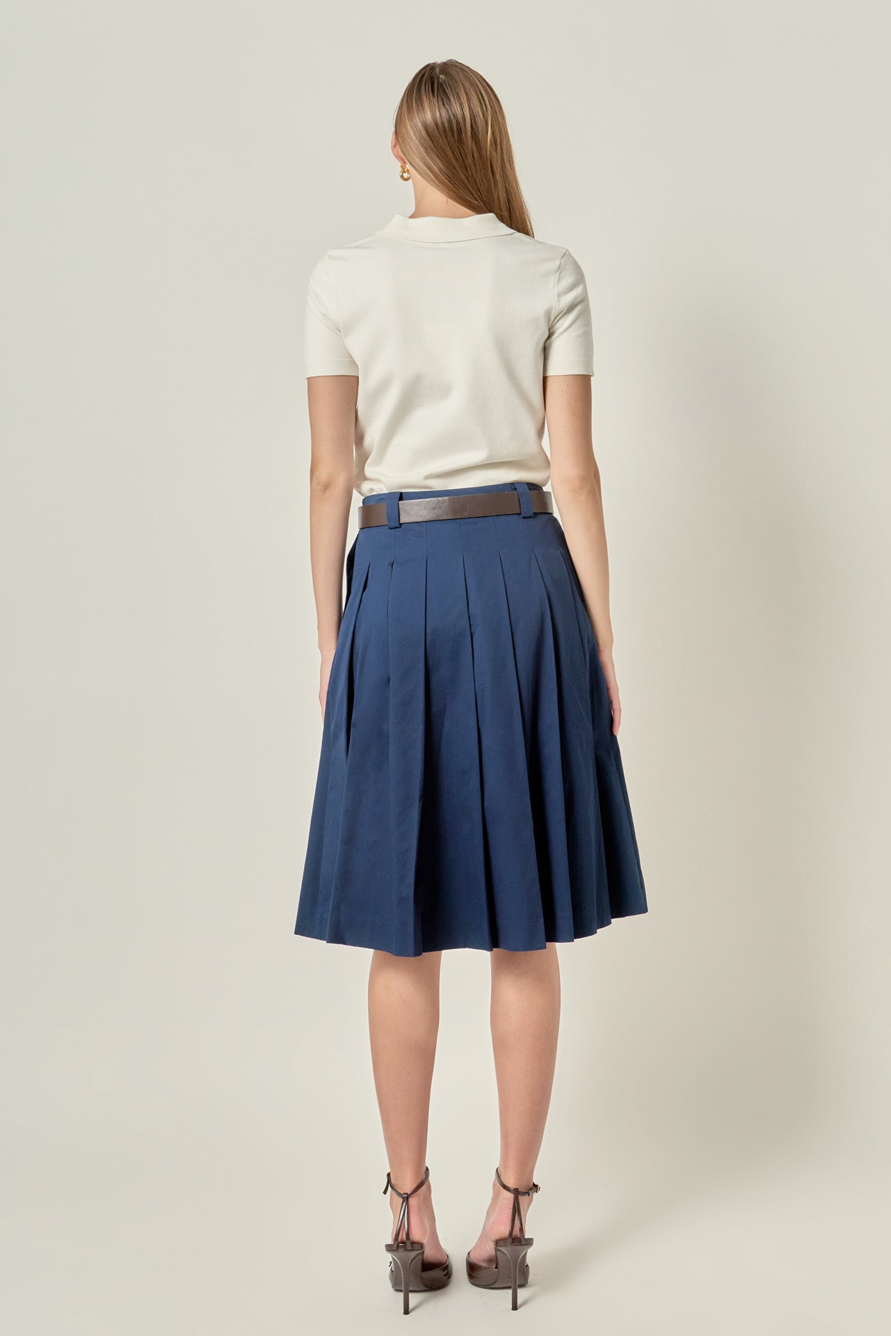 Straight-on rear view of a navy blue pleated midi skirt showing the continuous knife pleat construction and waist belt loops.