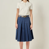 Full-length front view of a navy blue pleated cotton midi skirt featuring belt loops, styled with a cream short-sleeve polo shirt.