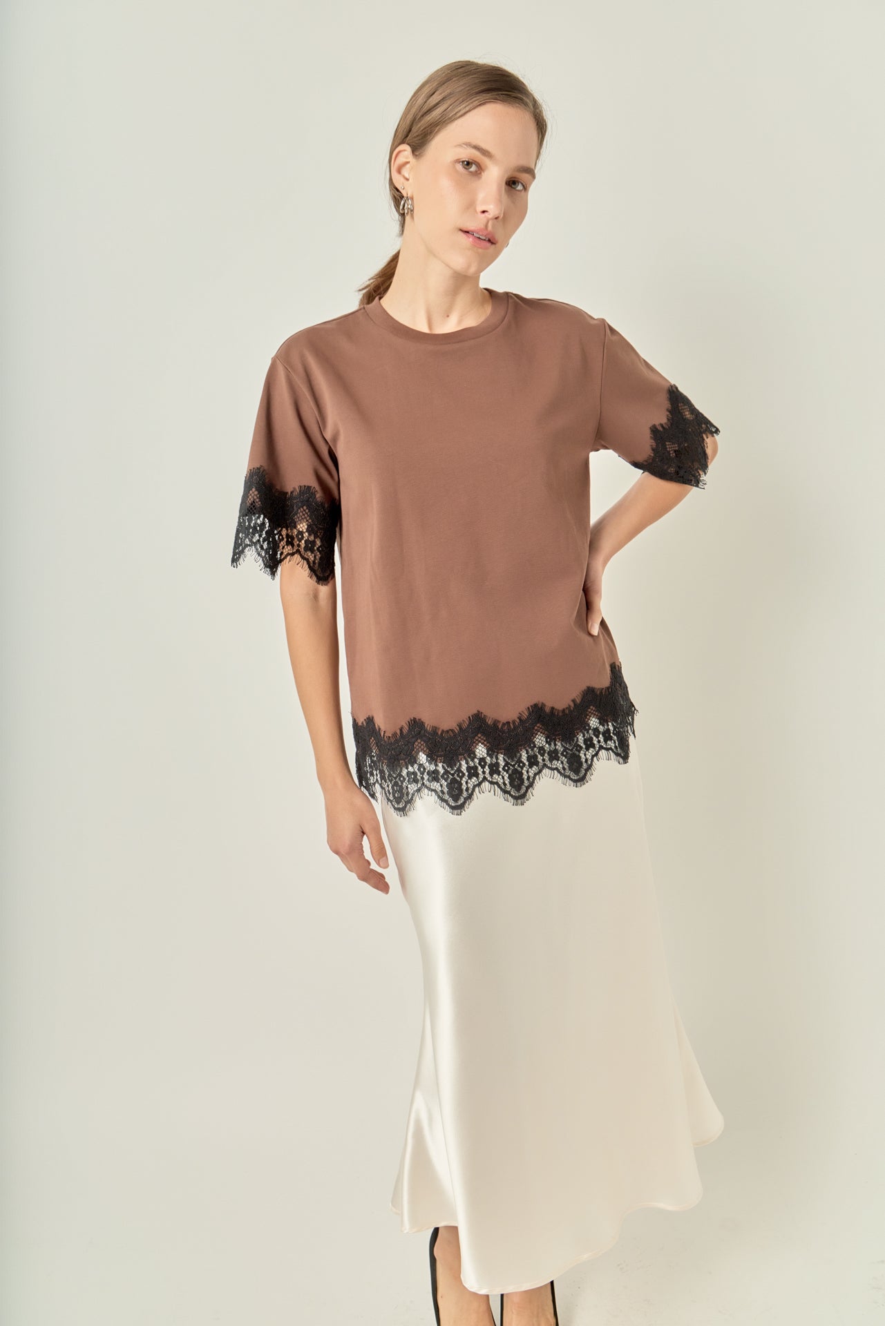 Face-forward posed view of a brown short-sleeve top with black lace trim showcasing the relaxed silhouette.