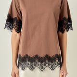 Upper body close-up view of a brown round-neck top highlighting the black contrast eyelash lace trim along the cuffs and hemline.