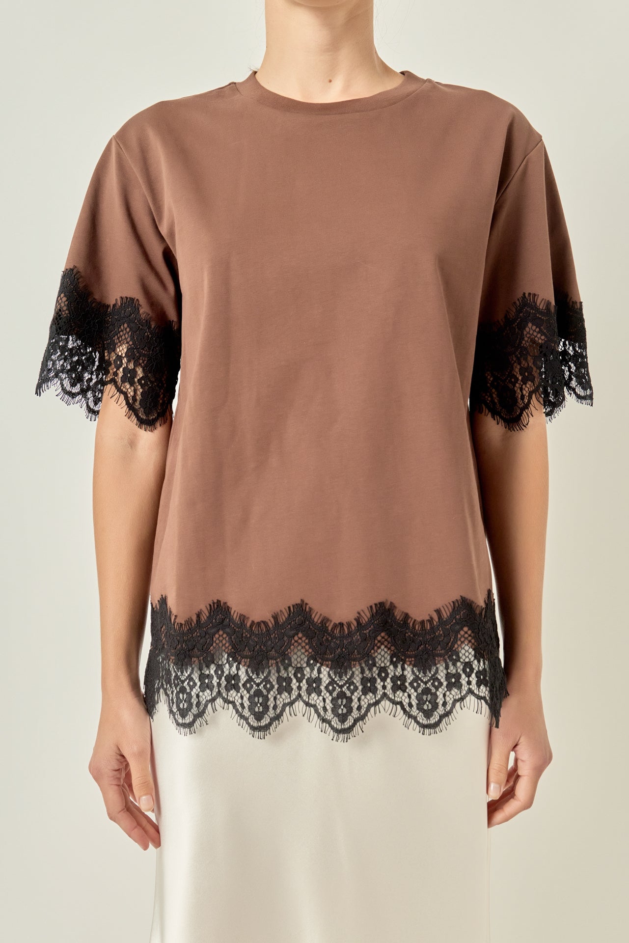 Upper body close-up view of a brown round-neck top highlighting the black contrast eyelash lace trim along the cuffs and hemline.