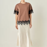 Full-length front view of a brown short-sleeve top featuring black contrast eyelash lace trim at the sleeves and hem, styled with a cream satin midi skirt.