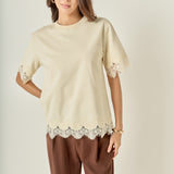 Face-forward posed view of a cream lace-trimmed short-sleeve top showcasing the effortless fit and tonal texture.