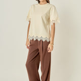 Side profile view of a cream short-sleeve top showing the straight side seam and scalloped lace cuffs.