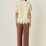 Straight-on rear view of a cream round-neck top displaying a smooth back profile and tonal lace trim at the bottom hem.