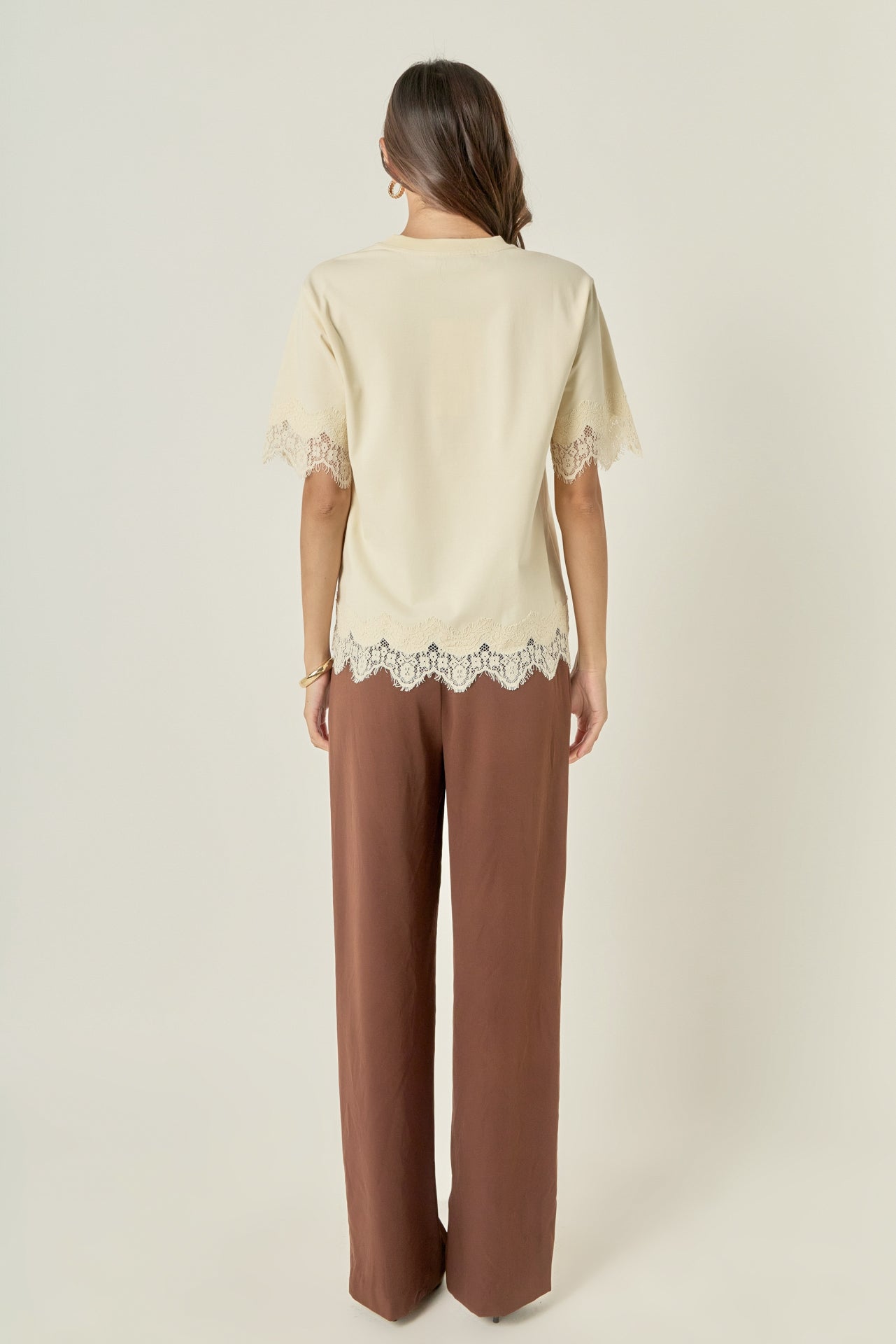 Straight-on rear view of a cream round-neck top displaying a smooth back profile and tonal lace trim at the bottom hem.