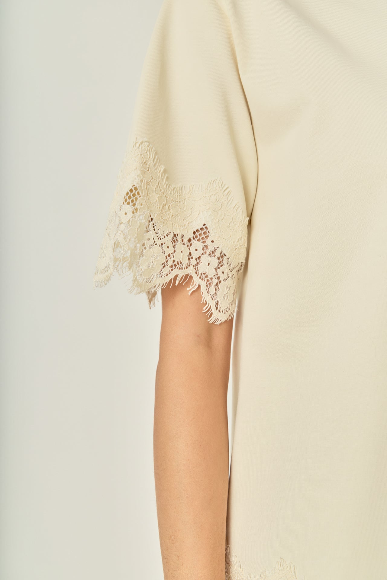 Ultra close-up detail view of cream cotton knit fabric with matching scalloped eyelash lace trim.