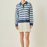 Full-length front view of a navy multi striped polo knit mini dress featuring a blue striped long-sleeve sweater bodice and a cream pleated skirt hem.