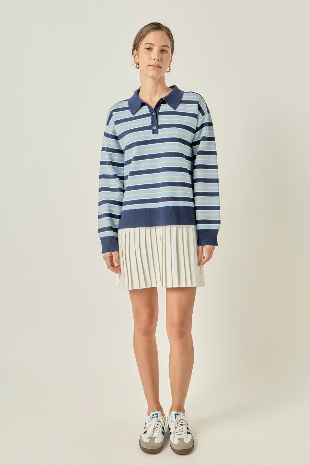 Full-length front view of a navy multi striped polo knit mini dress featuring a blue striped long-sleeve sweater bodice and a cream pleated skirt hem.
