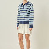 Side profile view of a navy multi striped polo knit mini dress showing the long sleeves and fluid drape of the cream pleated hem.