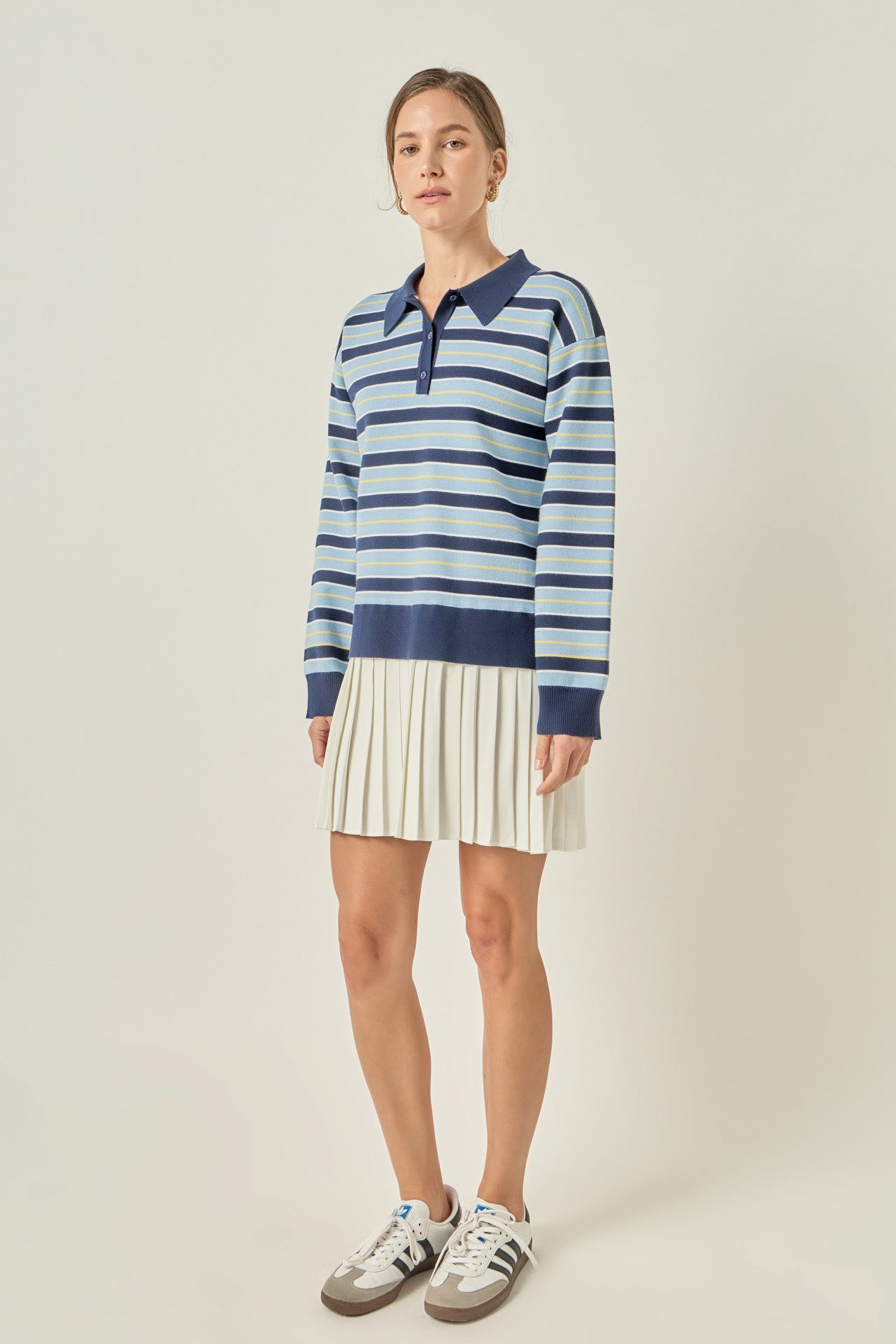 Side profile view of a navy multi striped polo knit mini dress showing the long sleeves and fluid drape of the cream pleated hem.