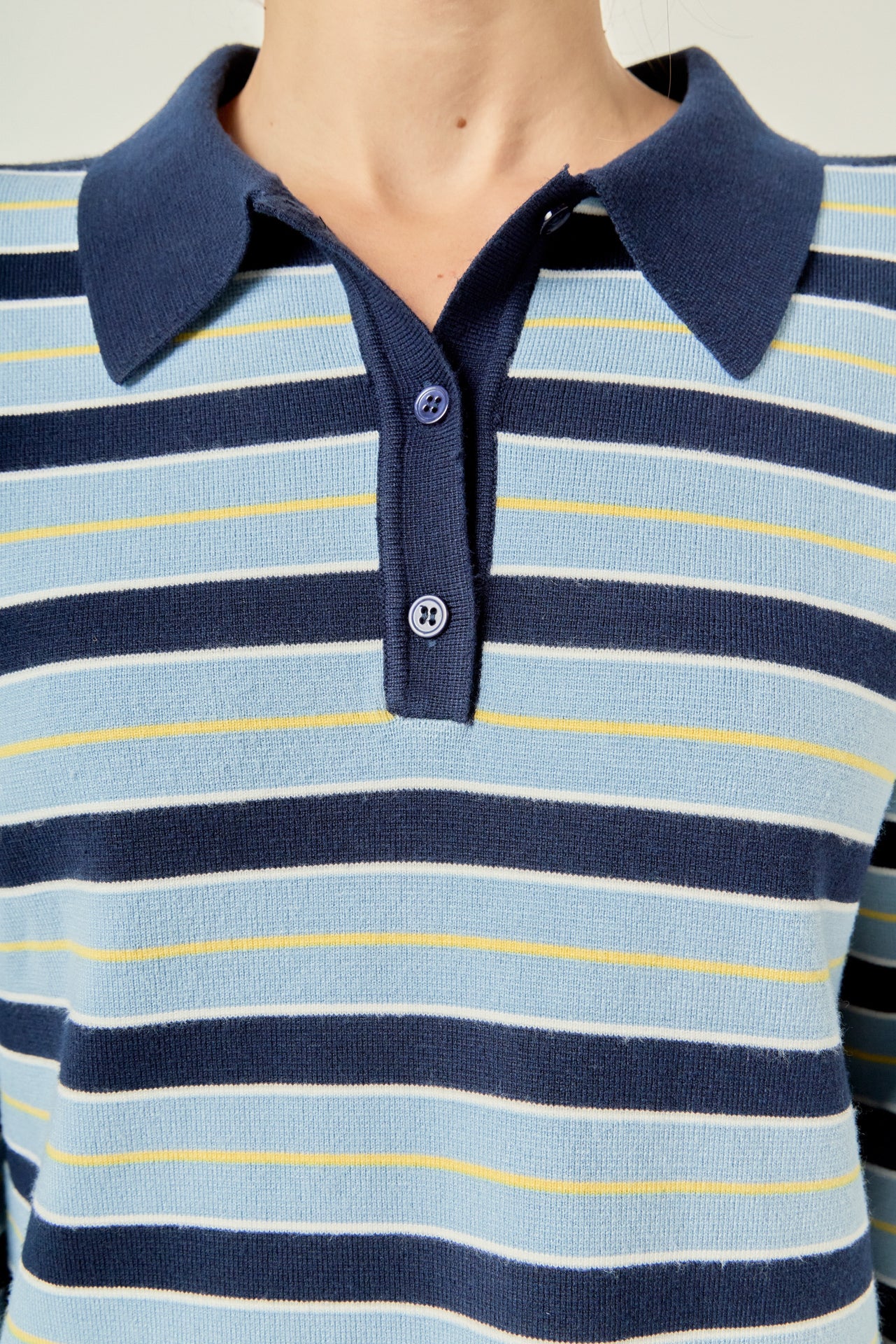 Ultra close-up detail view of blue striped knit sweater fabric layered over crisp cream pleated skirt fabric.
