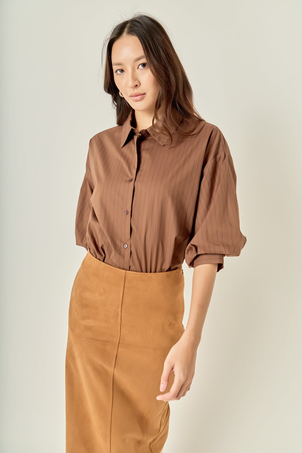 Three-quarter posed view of a brown pinstripe balloon sleeve shirt demonstrating the overall relaxed fit and sleeve drape.