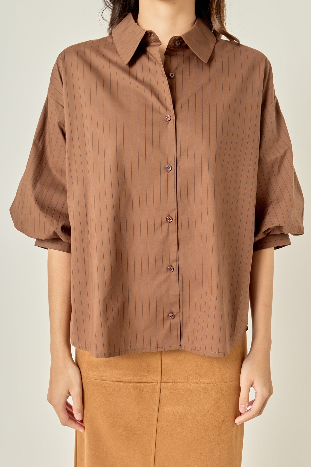 Waist-up untucked view of a brown pinstripe shirt highlighting the point collar, center-front button placket, and relaxed hemline.