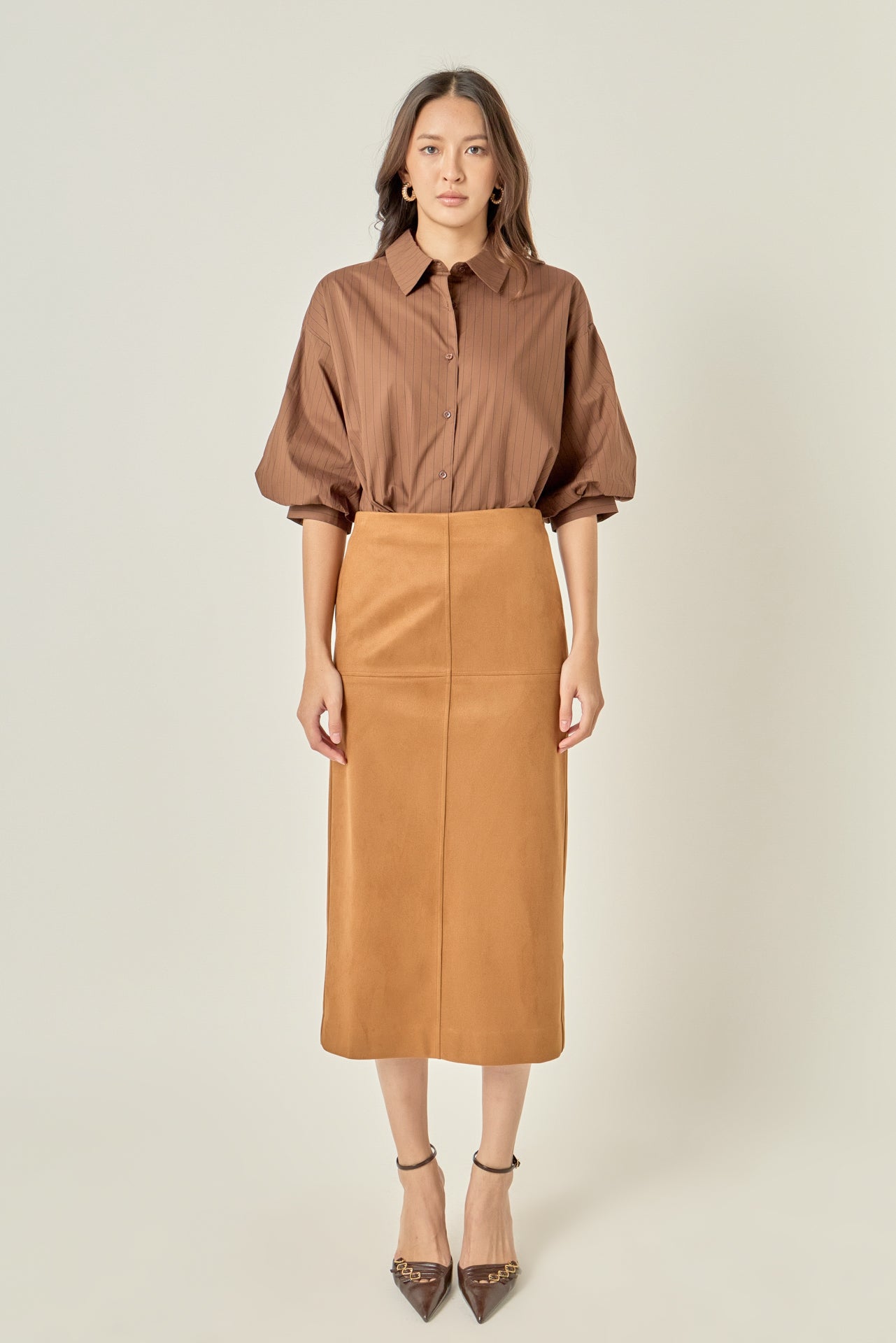 Full-length front view of a brown pinstripe button-down shirt featuring voluminous balloon sleeves, styled tucked into a tan midi skirt.