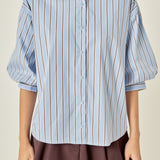 Waist-up untucked view of a dusty blue striped shirt highlighting the point collar, center-front button placket, and relaxed straight hem.
