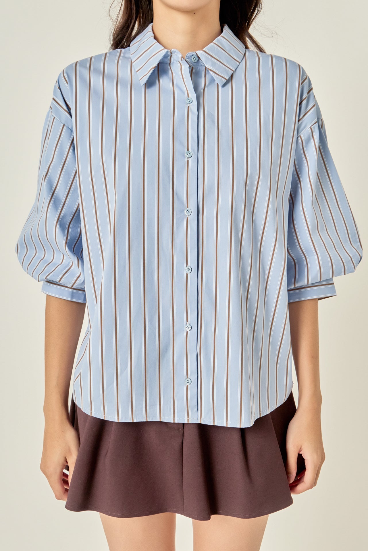 Waist-up untucked view of a dusty blue striped shirt highlighting the point collar, center-front button placket, and relaxed straight hem.