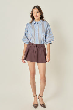 Full-length front view of a dusty blue striped button-down shirt featuring voluminous balloon sleeves, styled tucked into a brown pleated mini skirt.